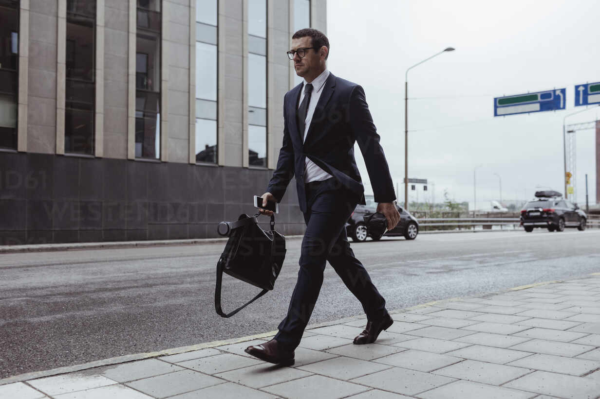 Affärsman med portfölj och smartphone i handen gående i stad